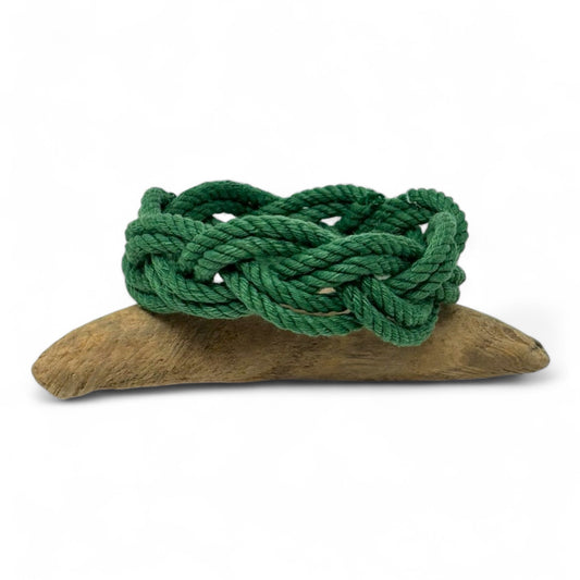 Green braided rope bracelet on a wooden base against a white background